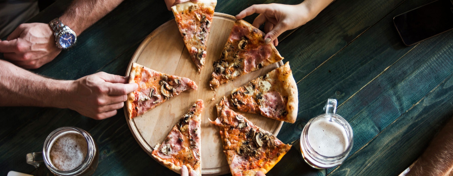 hands grab pizza slices around restaurant table