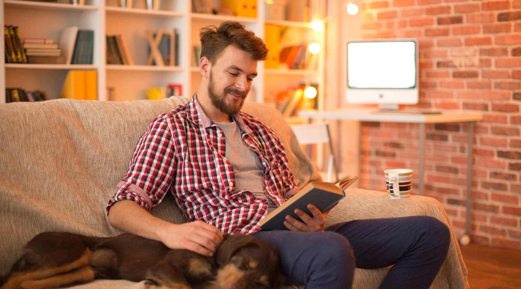 Historic charm, meet modern urban living young man sits on his couch reading a book next to his sleeping dog