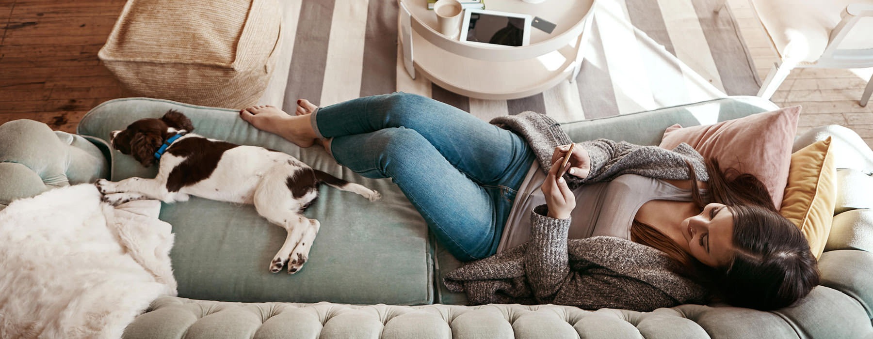 lady plays with her phone as she and her pup lounge on the couch